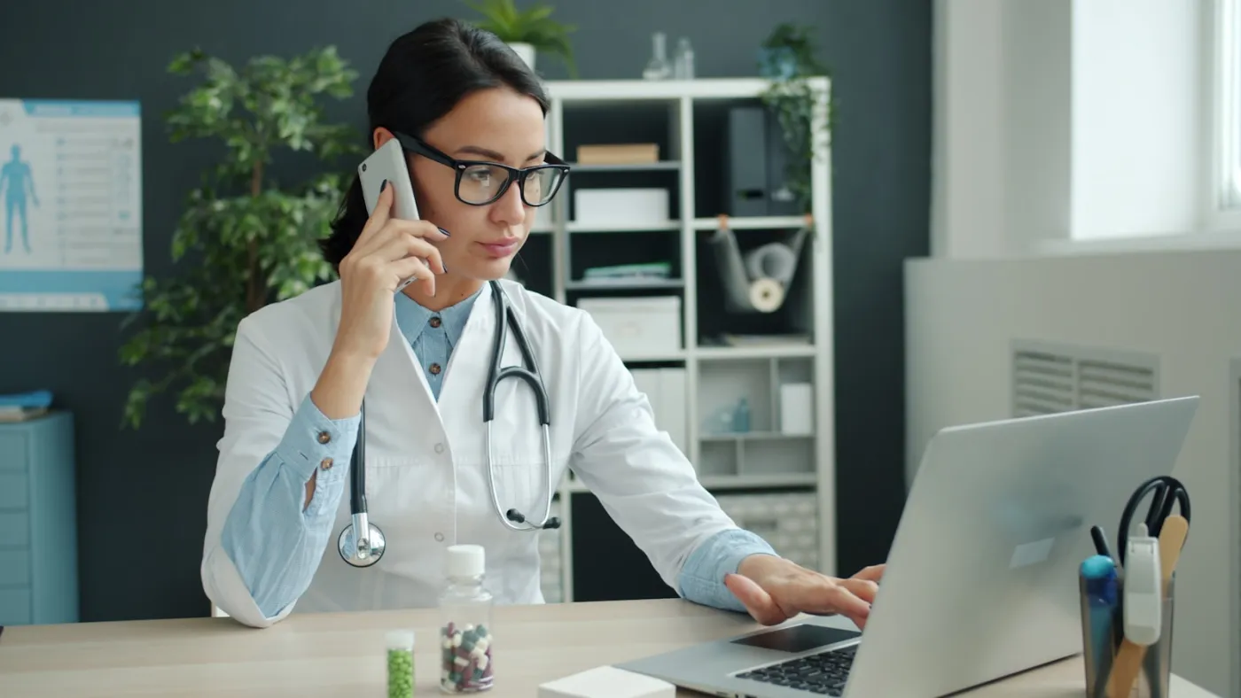Profesional de salud trabajando con una laptop en un entorno clínico.
