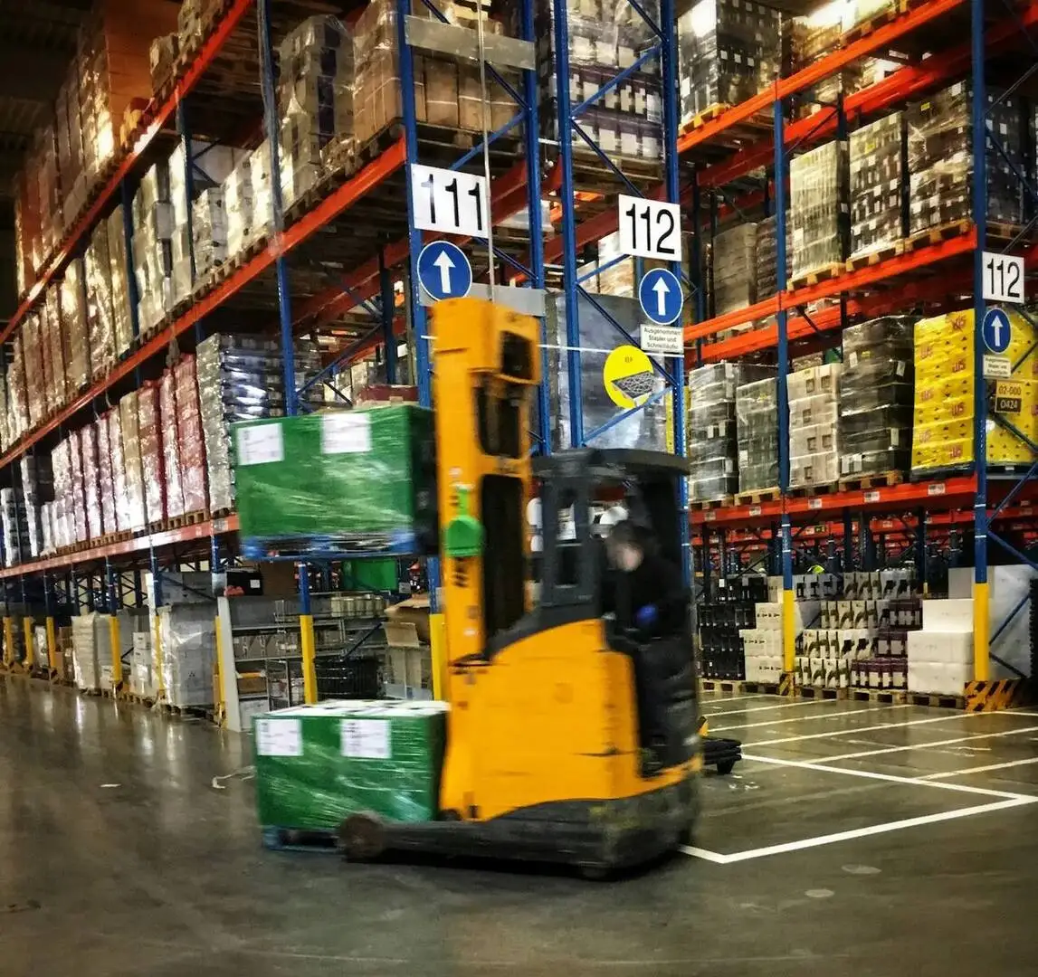 Operación logística en bodega con pallets y montacargas.